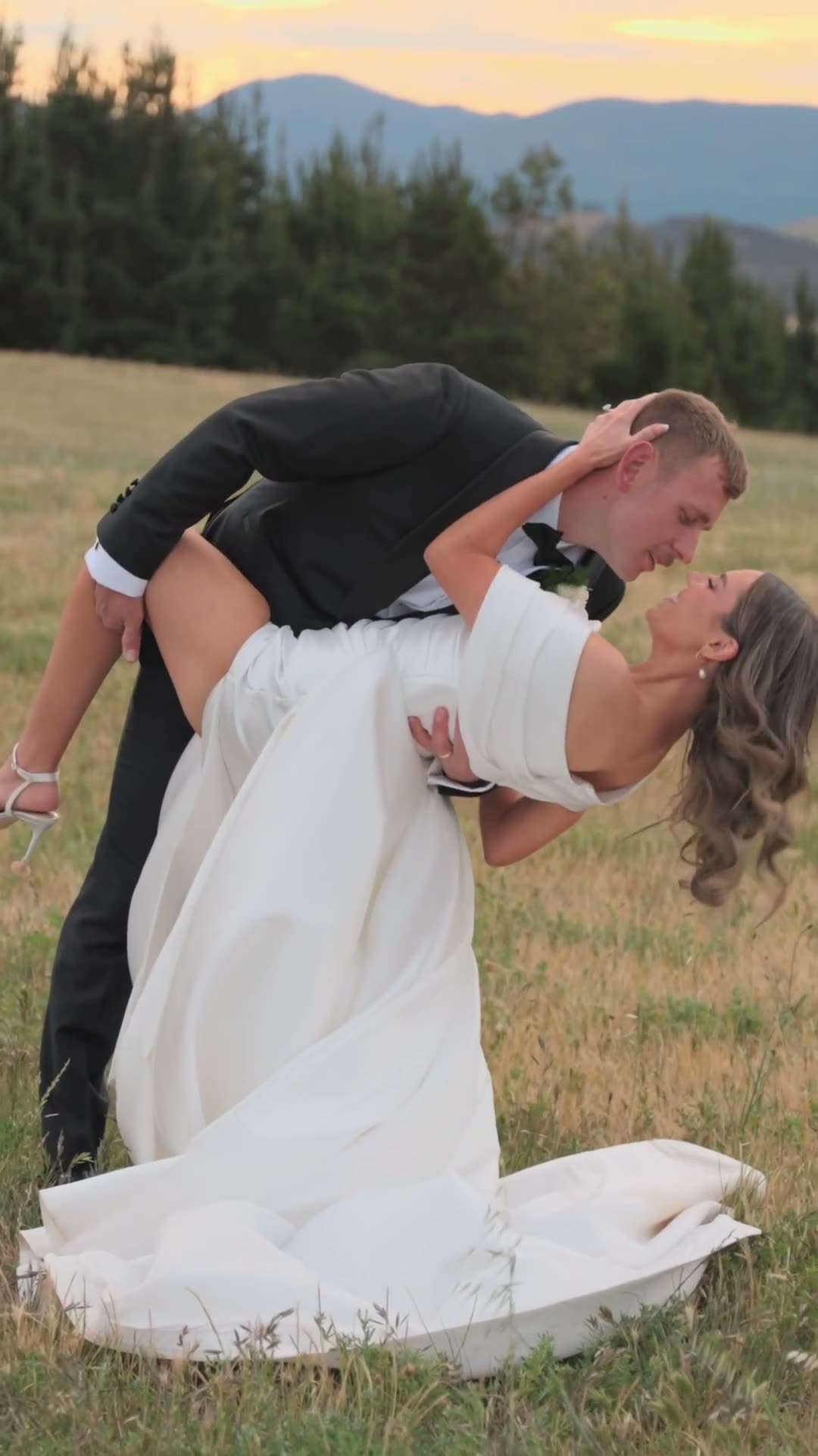 Taylah & Dylan. Thirty seconds, shot portrait. Opens on the couple's names set over a stone chapel, then a kiss with the ring in frame, a dip in a dry paddock, a red convertible, a black-and-white run toward a pine wall, and a lake at sunset.